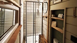 A narrow, compact bathroom with a wooden bench, a toilet, and a shower area with a sliding door.