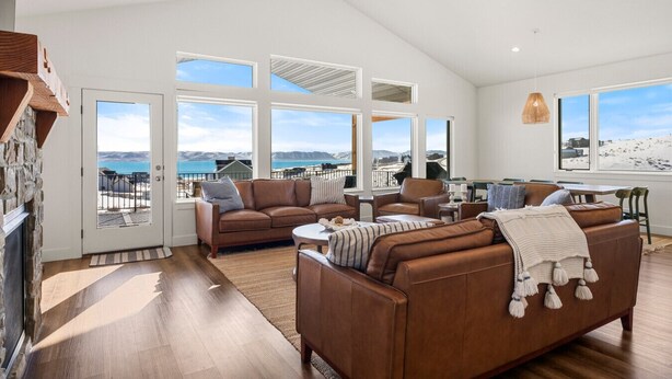 A spacious living room with a high ceiling, large windows offering a view of the sea, and a cozy seating area with leather sofas and a coffee table. - The Azure View - Sleeps 25 - Pickleball - POOL (Fish Haven)