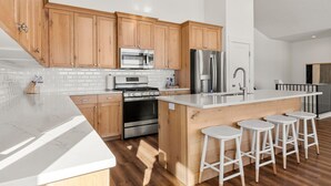 A modern kitchen with wooden cabinets, stainless steel appliances, a large island with stools, and a white countertop. - The Azure View - Sleeps 25 - Pickleball - POOL (Fish Haven)