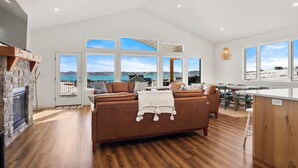 A spacious living area with a large window overlooking a scenic landscape, a cozy fireplace, and a wooden dining table. - The Azure View - Sleeps 25 - Pickleball - POOL (Fish Haven)