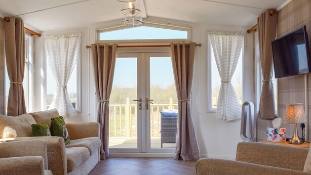 A room with a sofa, a TV, and a balcony with curtains.