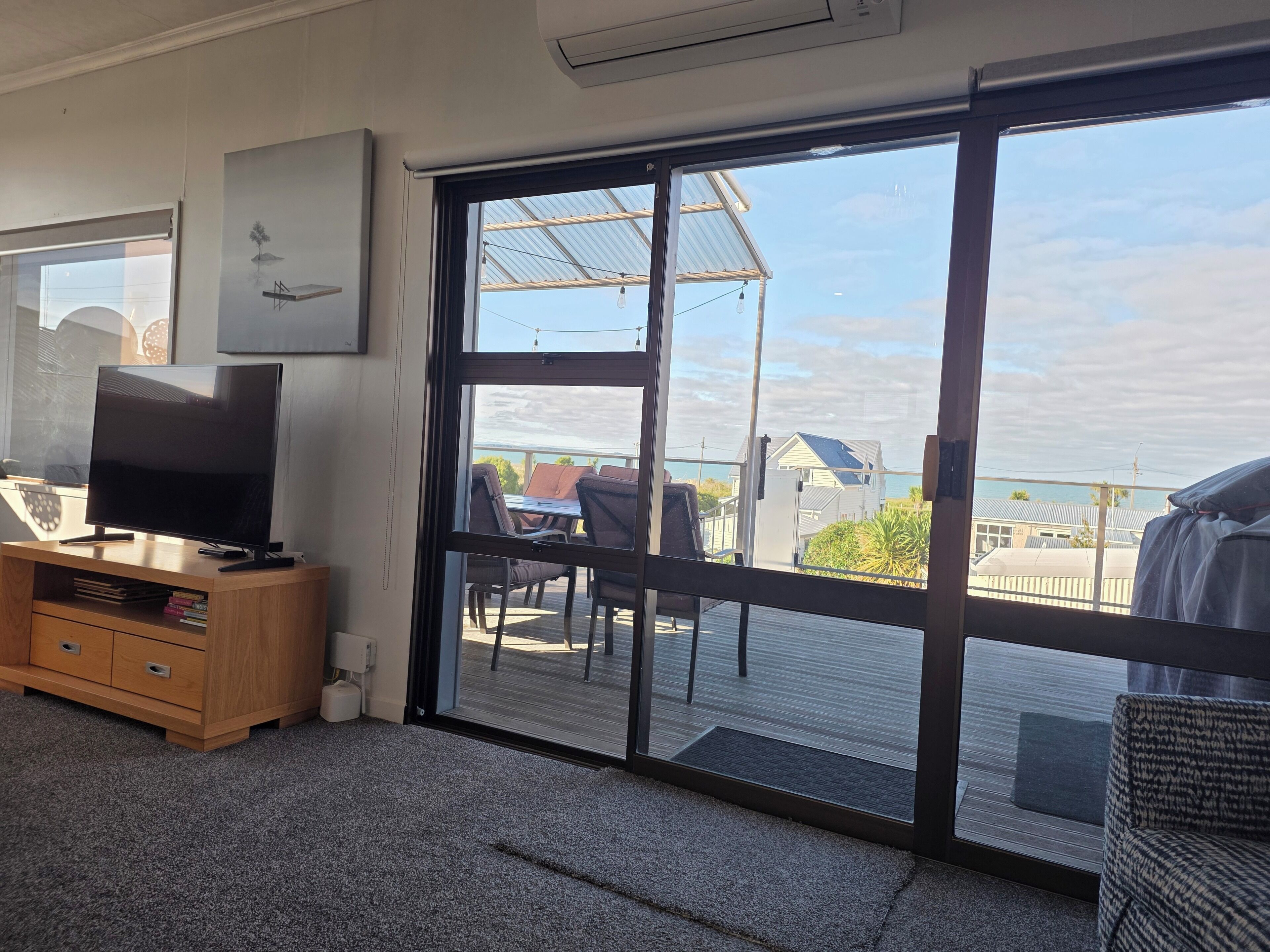 Ein Zimmer mit Fernseher auf einer Holzkabine, eine Schiebetür zu einem Außenbereich mit Tisch und Stühlen sowie Blick auf das Meer.