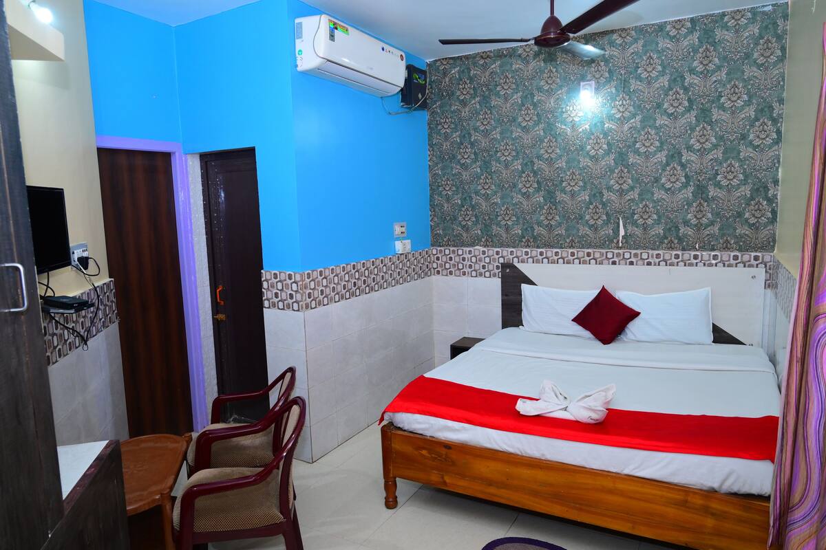Habitación de hotel con cama, escritorio, silla, aire acondicionado y ventilador de techo.