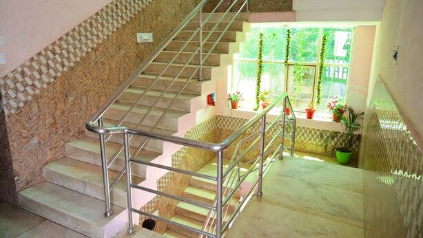A staircase with metal railings, a checkered wall pattern, and potted plants near a window. - DhamStay Hotel Beach Heaven Puri (Puri)