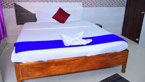 A neatly made bed with a blue bedspread, white linens, and a red pillow. - DhamStay Hotel Beach Heaven Puri (Puri)