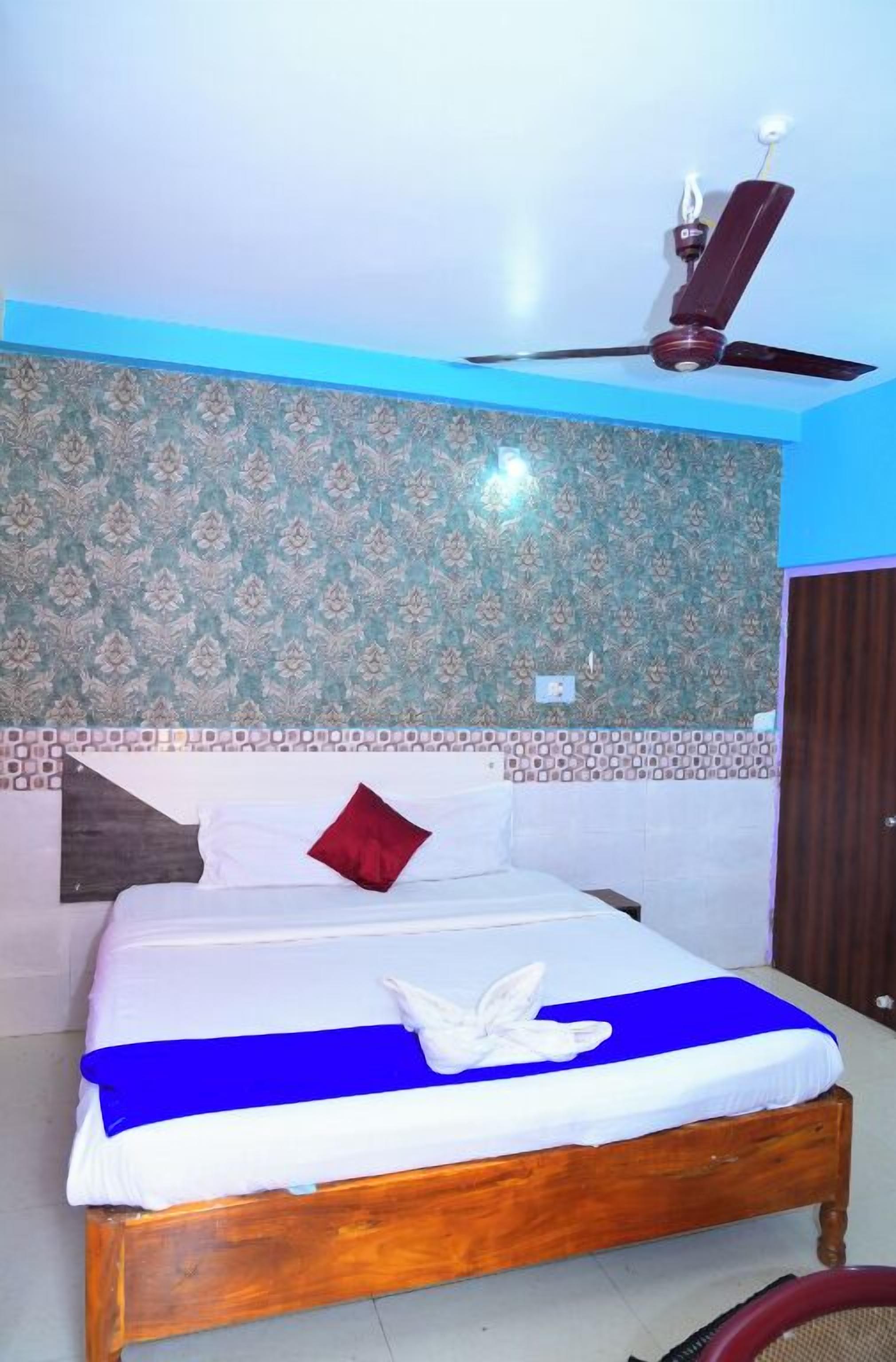 A neatly made bed with a blue and white bedspread, a red pillow, and a white towel on the bed.