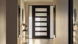 A hallway with a modern door, framed artwork on the walls, and a tiled floor.