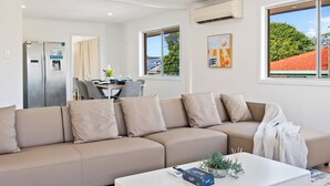 Ein modernes Wohnzimmer mit einem beigefarbenen Ecksofa, einem weißen Couchtisch und einem Essbereich mit Tisch und Stühlen.