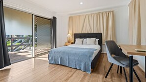 Ein Schlafzimmer mit Bett, Schreibtisch und Stuhl. Eine Glastür führt zu einem Außenbereich.