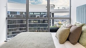 Un dormitorio con un ventanal grande, una cama y vistas a un paisaje urbano.