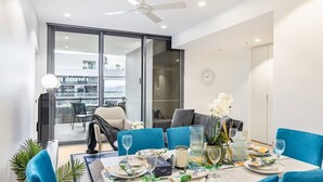 Comedor con una mesa dispuesta para cuatro, sillas azules y vista a un balcón exterior a través de un ventanal.