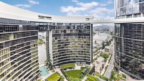Un edificio moderno con fachada de vidrio curva, una terraza en la azotea y vistas a un río y un puente.