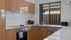 Eine moderne Küche mit Holzausstattung, einem Edelstahlherd, einem Backofen, einer Kaffeemaschine und einem Fenster mit Blick auf eine Backsteinmauer.