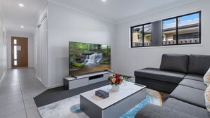 Ein modernes Wohnzimmer mit einem Flachbildfernseher, einem grauen Sofa und einem Couchtisch mit einer Blumenvase.
