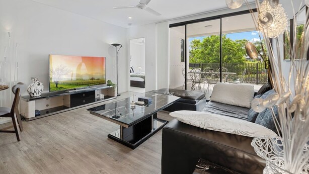 Una sala de estar moderna con una televisión de pantalla plana, una mesa de centro de vidrio, un sofá y una zona de comedor con sillas.