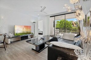 A modern living room with a flat-screen TV, a glass coffee table, a sofa, and a dining area with chairs. - Perfect Spot Near CBD & UQ | Spacious 2Beds Apt (Indooroopilly)