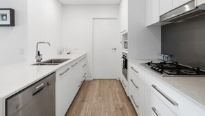 Una cocina moderna con armarios blancos, un lavamanos de acero inoxidable, lavavajillas, estufa y horno.