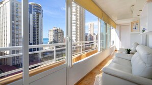 A modern apartment with large windows, a white sofa, and a view of tall buildings and the sea. - Apartment Oasis by Interhome (Calpe/Calp)