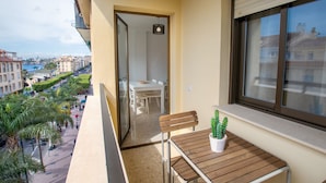 A balcony with a wooden table and chairs, a potted cactus, and a view of a cityscape with palm trees.