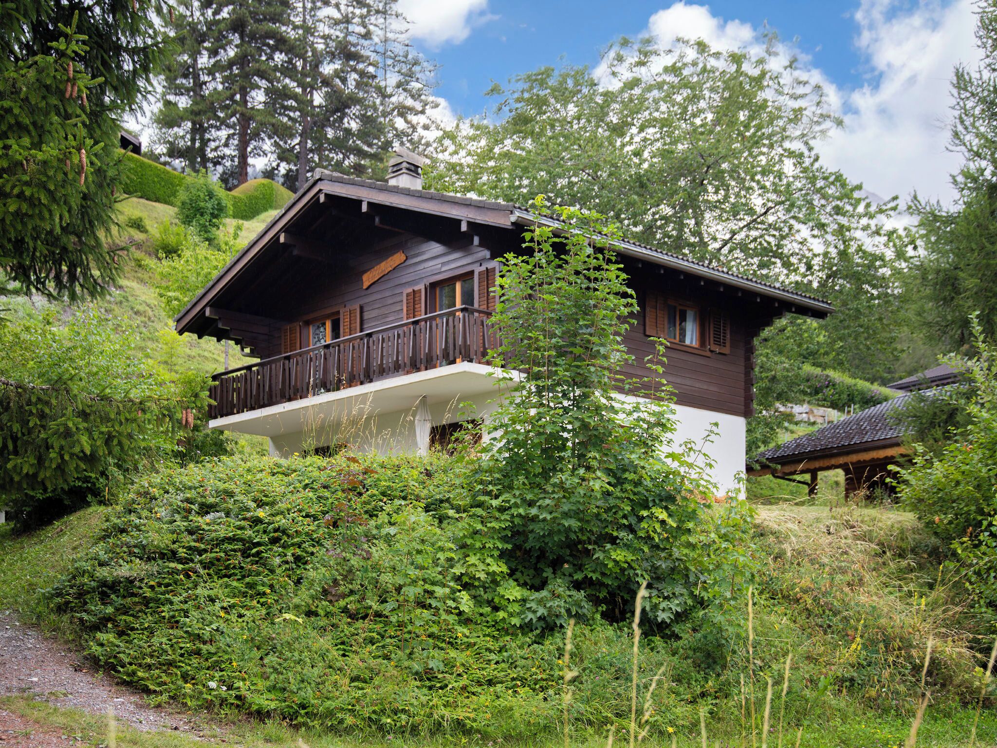 A chalet-style house with a balcony, surrounded by lush greenery and trees.