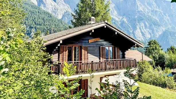 A chalet with a wooden exterior, a balcony, and a mountain backdrop.
