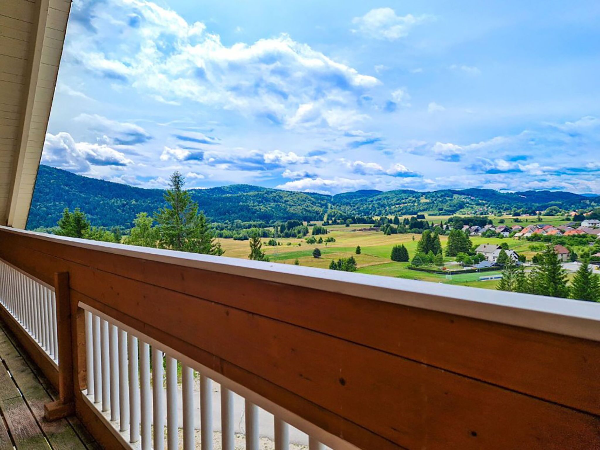 Un balcon doté d’une balustrade en bois, offrant une vue panoramique sur un paysage magnifique, avec des montagnes et un village.