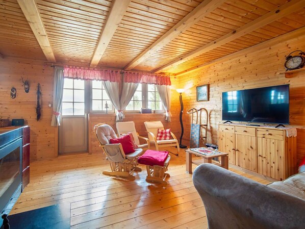 A cozy cabin interior with wooden walls and ceiling, a television, and a fireplace.