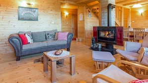A cozy wooden cabin interior with a sofa, a small table, a fireplace, and a dining area.