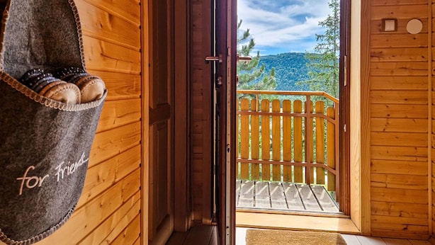 A wooden cabin with a balcony, a door with a 'for friends' sign, and a view of trees and hills.