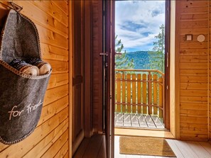 A wooden cabin with a balcony, a door with a 'for friends' sign, and a view of trees and hills.