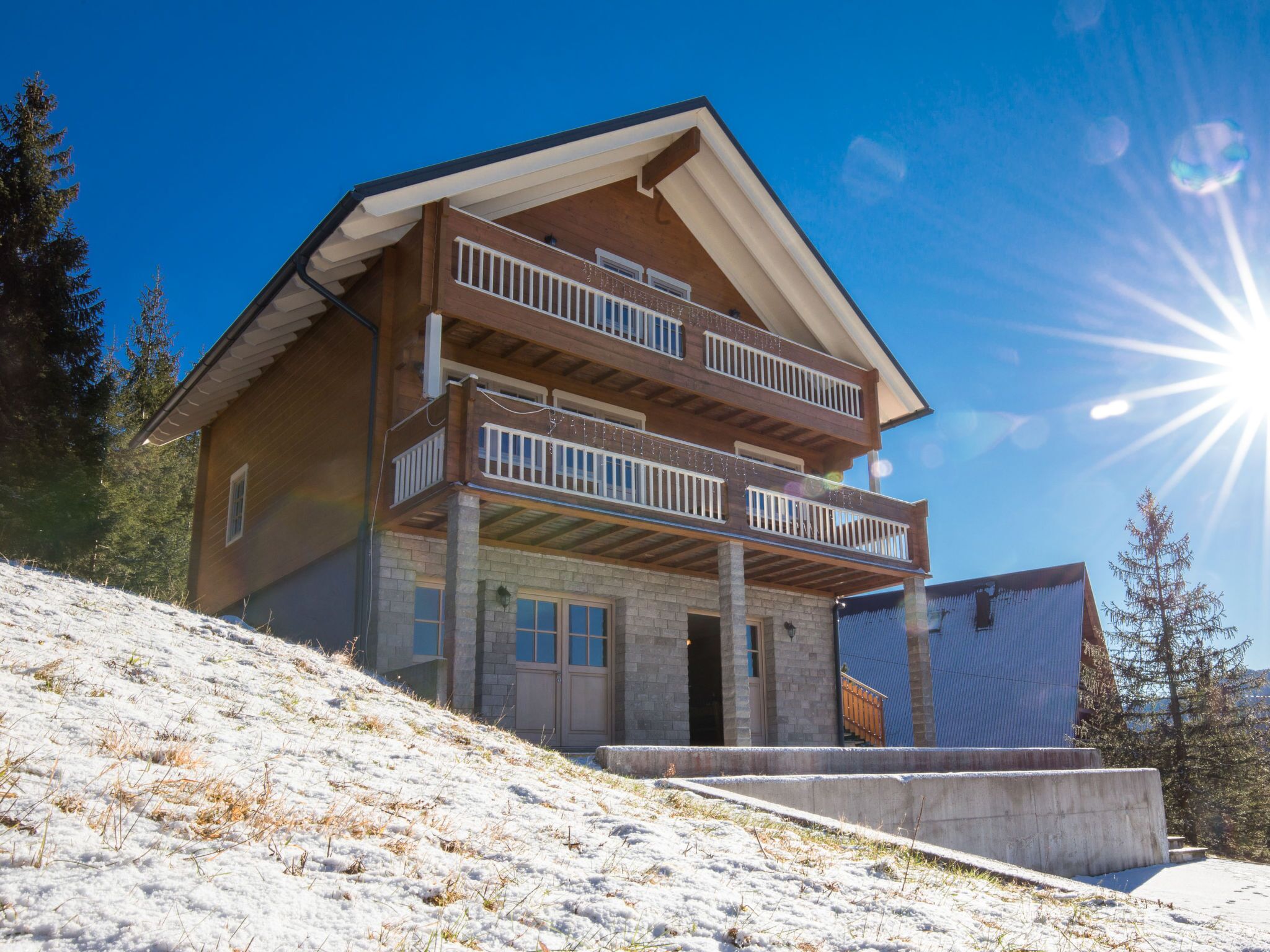 A two-story wooden house with a balcony, situated on a snowy slope.