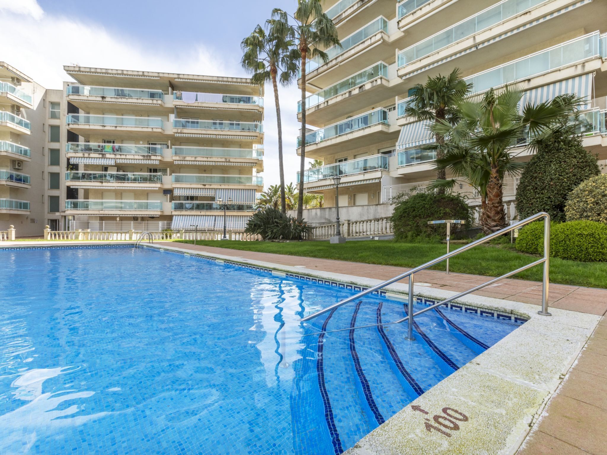 A swimming pool with clear blue water, surrounded by a tiled deck.