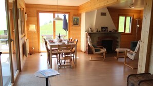 Amplia sala de estar con suelo de madera, una mesa de comedor preparada para seis personas y una chimenea.
