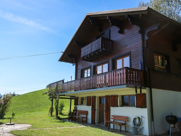 A two-story wooden chalet with a balcony, a covered porch, and a stone pathway leading to the entrance.