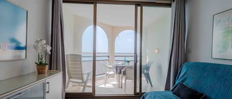 A balcony with a view of the sea, a sofa, a dining table, and chairs.