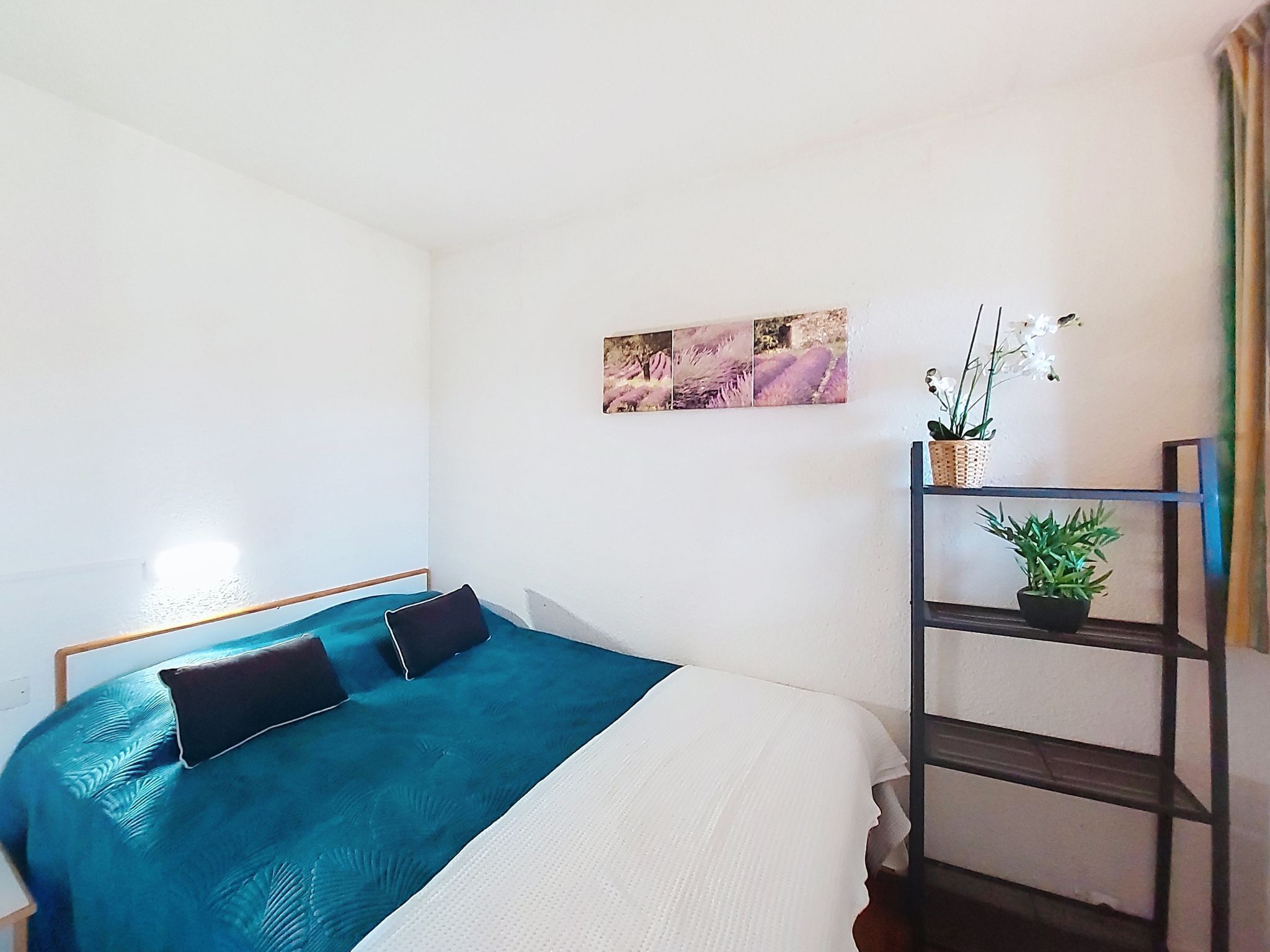 Une chambre à coucher avec un lit, une étagère ornée de plantes et un tableau accroché au mur.