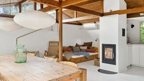 Ein gemütliches Zimmer mit Holzbalkendecke, einem weißen Sofa mit Kissen, einem kleinen Tisch mit einer grünen Vase und einem Kamin.
