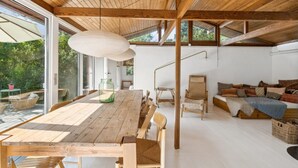 Ein geräumiges Zimmer mit einem Holzessttisch, Stühlen, einer Couch und einem großen Fenster mit Blick ins Freie.