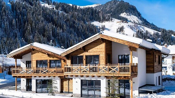A two-story wooden chalet with a balcony, large windows, and a view of snow-covered mountains. - Apartment in Kleinarl near Ski Slopes (Kleinarl)