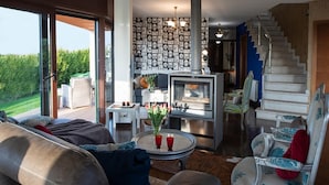 Un salón amplio con una chimenea grande, asientos cómodos y una escalera que sube a un nivel superior.