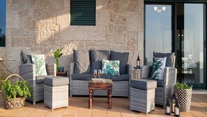 Un muro de piedra con un conjunto de sofás, una mesa de madera con vasos y plantas en macetas.