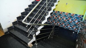 Een trap met zwarte marmeren treden en metalen leuningen, die leidt naar een kamer met een gele muur en een kleurrijk betegeld deel.