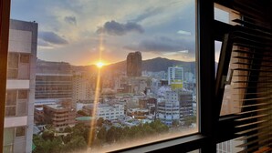 A cityscape with a sunset view through a window with blinds. - Available for up to 30 people 4-bedroom apartment in enchanting Busan with WiFi (Busan)