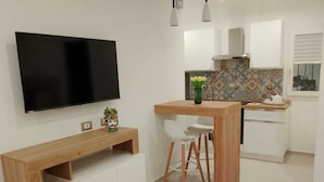 A modern kitchen with a wooden dining table, white chairs, a TV mounted on the wall, and a colorful backsplash.