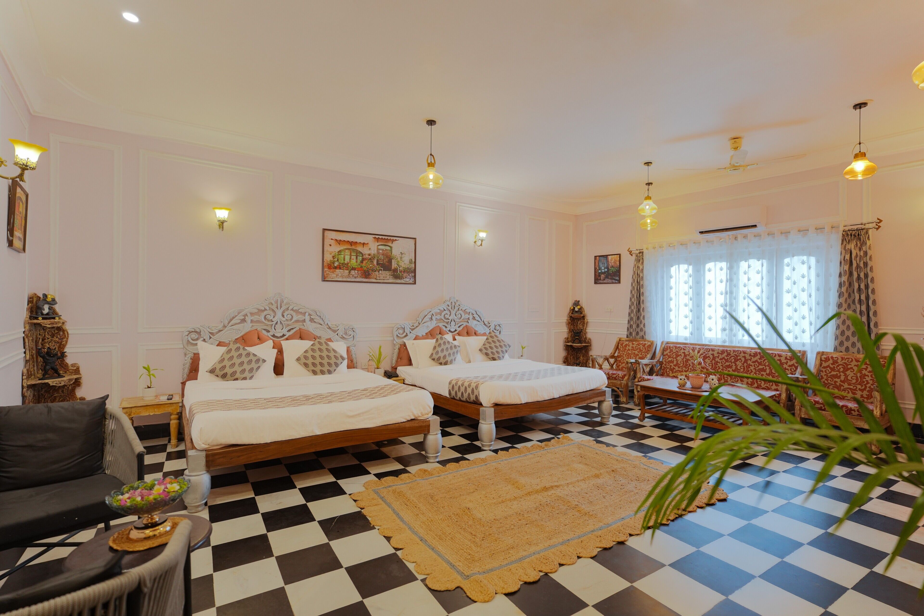 Habitación de hotel con dos camas, piso de cuadros, un ventanal con cortinas y un rincón de descanso con sofás estampados.