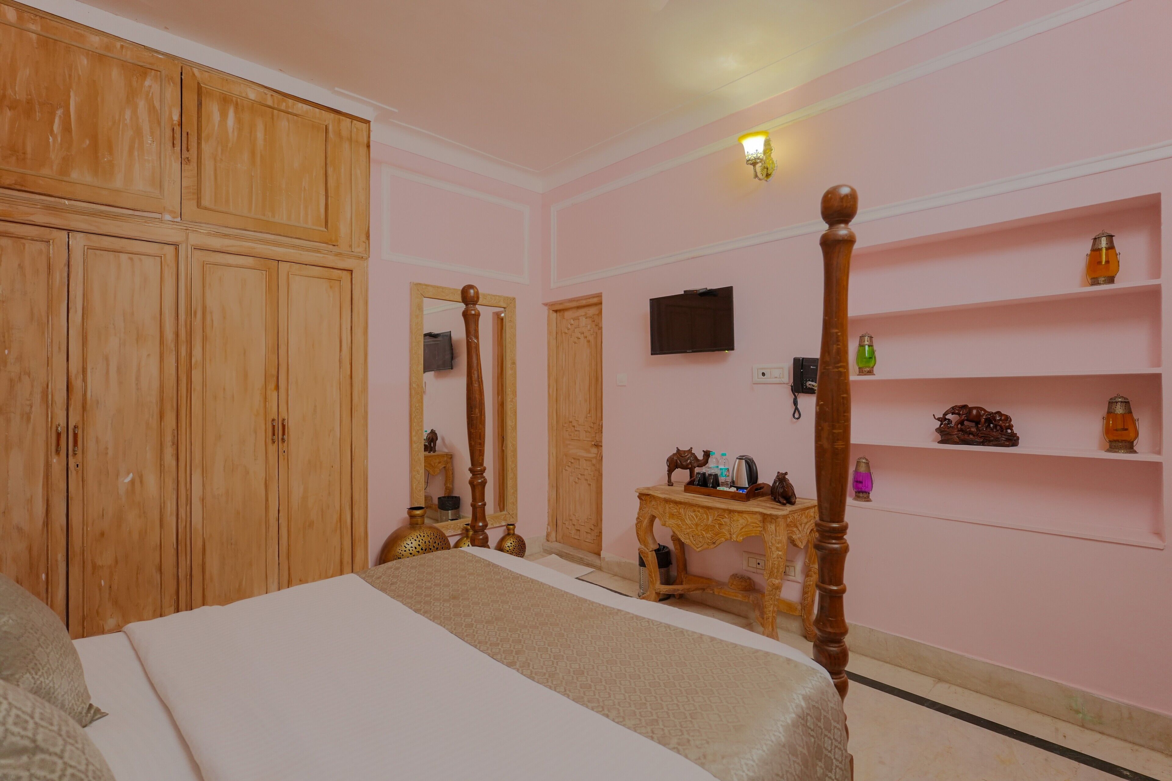 Une chambre à coucher comprenant un lit, une armoire en bois, un miroir, une télévision et une petite table agrémentée d’objets décoratifs.