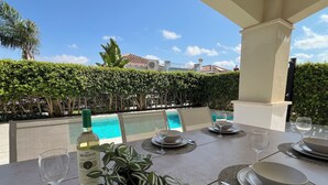 Une table à manger dressée avec des assiettes, des bols, des verres à vin et une bouteille de vin, donnant sur une piscine.