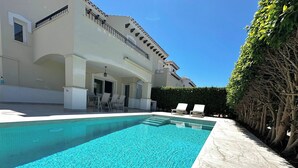 Une piscine à l’eau d’un bleu cristallin, entourée d’un bâtiment blanc doté de balcons et d’une haie.