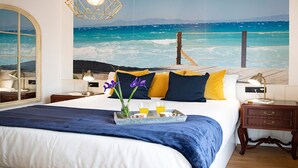 Ein Schlafzimmer mit einem großen Bett, einem Nachttisch, einer Lampe, einem Tablett mit Getränken und einem Wandbild von einem Meer.