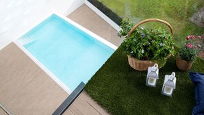 Ein Poolbereich mit Holzterrasse, einer kleinen Rasenfläche mit Blumentöpfen und zwei Laternen.